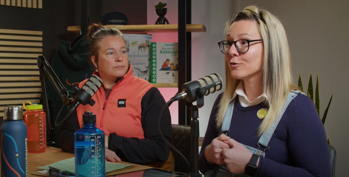 Deux femmes participant à une discussion en podcast autour d'une table d'accueil équipée de microphones et de bouteilles d'eau, entourées de plantes d'intérieur et d'objets décoratifs en arrière-plan.